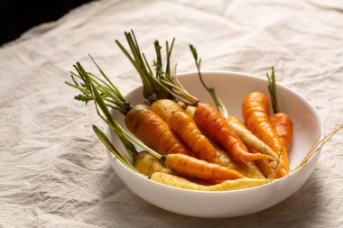 Beyaz, sarı ve turuncu havuçlar beyaz bir kasede, masa örtüsünün üzerinde. Çeşitli sebze konsepti