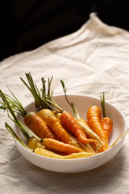 Beyaz, sarı ve turuncu havuçlar beyaz bir kasede, masa örtüsünün üzerinde. Çeşitli sebze konsepti