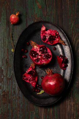 Tahta arka planda siyah metal bir tepside sulu nar meyvesi aç. Kırsal tarzda sade bir fotoğraf.