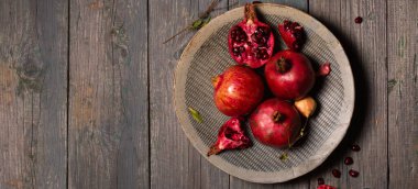 Olgun sulu nar bütün ve gri ahşap arka planda seramik gri bir tabakta açılır. Kırsal tarzda bir fotoğraf.