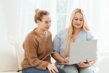 Kanepede oturmuş laptopa bakan iki kadın. İçlerinden biri gözlük takıyor. Laptop açık ve ona bakıyorlar.