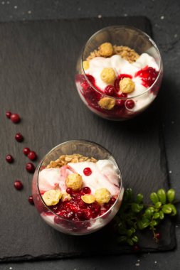 Siyah bir masada iki bardak yaban mersinli, yoğurtlu ve tahıllı tatlı.