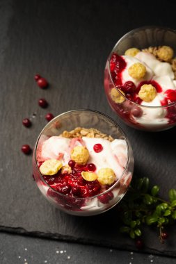 Siyah bir masada iki bardak yaban mersinli, yoğurtlu ve tahıllı tatlı.