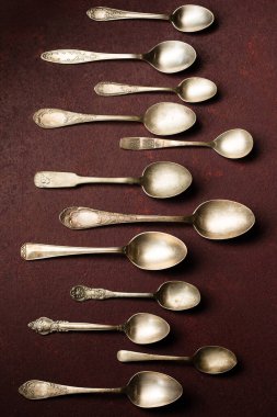 Bordo bir arka planda sırayla dizilmiş eski kaşık koleksiyonu. Üst görünüm