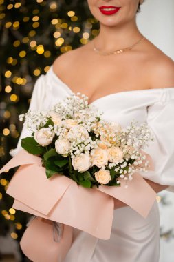 Bir kadın elinde bir buket çiçekle bir Noel ağacının önünde duruyor. Sahne şenlikli ve neşeli, kadının kırmızı ruju resme renk katıyor.