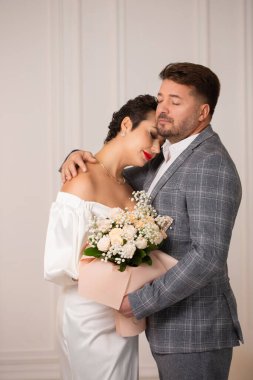 Damat geline nazikçe sarıldı. Gelin elinde bir buket pembe gül tutuyor..