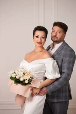 Gelin ve damat, gelinin elinde bir buket çiçekle poz veriyorlar.