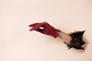 Deri eldivenli bir kadının eli bir jest gösterir. El, bej kağıttaki bir delikten itilir..