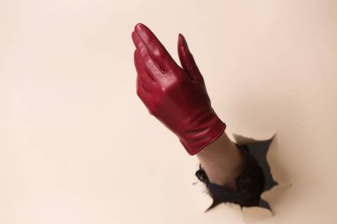 Deri eldivenli bir kadının eli bir jest gösterir. El, bej kağıttaki bir delikten itilir..