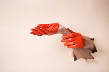 Deri eldivenli bir kadının elleri bir jest gösterir. Elleri bej kağıttaki bir delikten itiliyor..