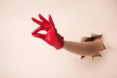 Deri eldivenli bir kadının elleri bir jest gösterir. Elleri bej kağıttaki bir delikten itiliyor..