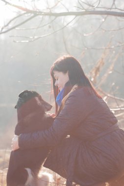 Güneşli bir günde ilkbaharın başında köpeğini kucaklayan bir kadın.