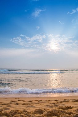 Okyanus kıyısındaki sahil boş ve gökyüzü mavi. Güneş ışıl ışıl parlıyor ve su sakin.