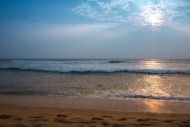 Okyanus sakin ve gökyüzü mavi. Güneş suyun üzerinde parlıyor, güzel bir yansıma yaratıyor.