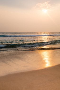Güneş okyanusun üzerinde batıyor, kumun üzerine sıcak bir parıltı saçıyor. Su sakindir ve gökyüzü turuncu ve pembe renklerin bir karışımıdır. Sahne huzurlu ve huzurlu.