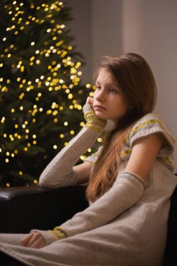 Düşünceli, üzgün genç kız, Noel ağacının yanında oturur. Sıcak kışlık giysiler giyer ve Noel 'in gelmesini bekler.