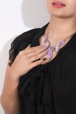 Siyah elbiseli ve mor kolyeli bir kadın. Manikürü kolyeye uyuyor.