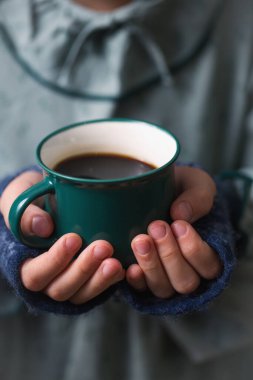 Yünlü eldivenlerde çocukların elleri sıcak bir içecekle yeşil bir kupa tutuyor, yakın plan.