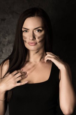 Siyah kolsuz tişörtlü güzel bir kadın karanlık arka planda vücuduna askeri makyaj uyguluyor.