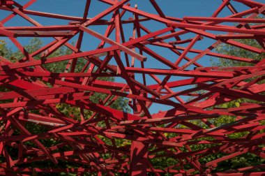 Temiz bir gökyüzüne karşı kırmızı metal kirişlerin geometrik bileşimi. Arkasında binalar olan bir inşaat kaosu görebilirsiniz.