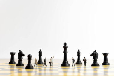 Satranç tahtasındaki minyatür insanlar iş stratejisini ve takım dinamiğini sembolize ediyor.