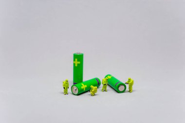 Yeşil bataryaların etrafına yerleştirilmiş küçük biblolar, takım çalışması veya enerji tasvir ediyor.