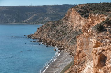 Turkuaz deniz suyu güneşli bir günde kayalık uçurumun aşağısındaki Doğu Pissouri sahilinde tur atıyor. Limasol İlçesi, Kıbrıs