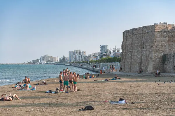 stock image Larnaca, Cyprus - September 07, 2019: Tourists relaxing at Finikoudes beach with a Larnaca Castle nearby