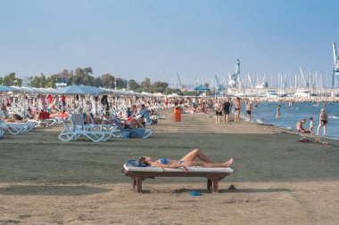 Larnaca, Kıbrıs - 07 Eylül 2019: Kadın Finikoudes plajındaki ahşap bir bankta güneşleniyor