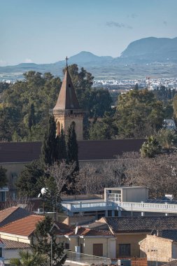 Terracotta çatısı olan geleneksel evlerin üzerinden Kutsal Haç Kilisesi kulesine ve uzaktaki Pentadactylos dağlarına bakın. Kıbrıs