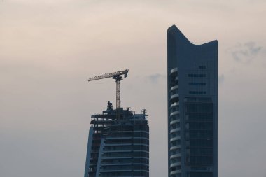 İnşaat vinci, Kıbrıs 'ın Limasol kentinde gün batımında bulutlu bir gökyüzüne karşı modern bir gökdelen inşa ediyor.