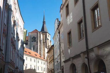Prag, Çek Cumhuriyeti 'nde üzerinde bir kilise kulesi yükselen dar bir sokakta geleneksel binalar.