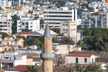 Bayraktar Camii 'nin minaresi, binalar ve palmiye ağaçlarıyla dolu bir siluetten görünüyor. Lefkoşe, Kıbrıs