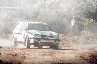 Anogyra, Limasol Bölgesi, Kıbrıs Rum Kesimi - 29 Ocak 2023: Volkswagen Golf III Ralli aracı toprak bir yolda hızla giderken tozlanıyor ve Anogyra Ralli 2023 arka planında bir izleyici izliyor.