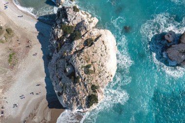 Rocky shore of Petra tou Romiou (Aphrodite's Rock) with tourists enjoying the beach on a sunny day. Paphos District, Cyprus clipart