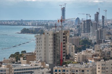 Güneşli bir günde deniz kenarında modern binalarda çalışan vinçler.