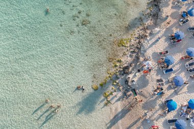 Turistler plajda dinlenerek ve okyanusta yüzerek yaz tatilinin tadını çıkarıyorlar.