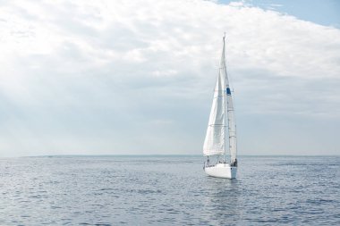 Bulutlu bir günde arka planda adayla denizde yelken açan beyaz yelkenli.