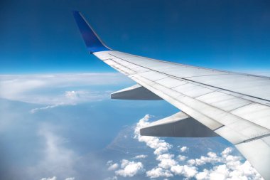 Pofuduk bulutların üzerinde süzülen uçak kanatları güneşli bir günde mavi gökyüzüne karşı seyahat, özgürlük ve yaz tatillerini çağrıştırıyor.