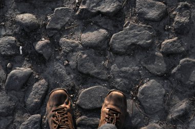 Gezgin, kahverengi yürüyüş botlarıyla kaldırım taşı bir yolda duruyor, keşfe ara veriyor.