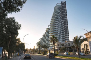 Limasol, Kıbrıs - 3 Ocak 2024: Modern gökdelen, Kıbrıs Rum Kesimi 'nin Limasol kıyı şeridinde yol boyunca giden arabalarla dimdik ayakta duruyor