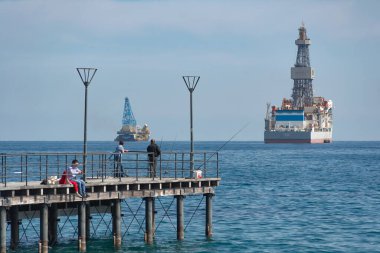 Limasol, Kıbrıs - 5 Mart 2019: Arka planda petrol platformuyla iskelede balık tutan insanlar