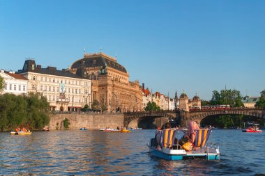 Prag, Çek Cumhuriyeti - 19 Mayıs 2015: Turistler güneşli bir yaz gününün tadını çıkarıyorlar, Ulusal Tiyatro ile Vltava Nehri 'nde bir pedal teknesine biniyorlar ve arkada Prag, Çek Cumhuriyeti' nde bir köprü var.