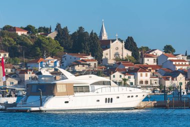 Lüks beyaz yat, rogoznica, Hırvatistan 'ın sakin limanına demirlemiş, büyüleyici yamaç köyü ve önde gelen kilisesi de arka planda.