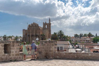 Senior tourist couple admiring Lala Mustafa Pasha mosque (Cathedral of Saint Nicholas) from the ancient venetian walls in Famagusta, Cyprus, on a sunny day clipart