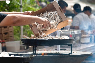 Şef açık hava yemek festivalinde taze istiridye mantarları kızartarak vejetaryen yemeği hazırlıyor.