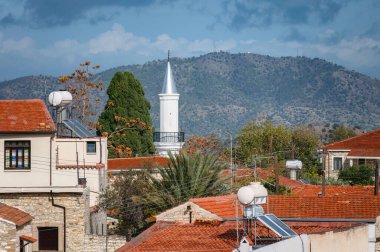 Kıbrıs Rum Kesimi 'nin Pano Lefkara köyünde bir dağ zeminine karşı duran kırmızı kiremit çatılı geleneksel Kıbrıs evleri ve Hamidiye Camii' nin beyaz bir minaresi. Larnaca Bölgesi