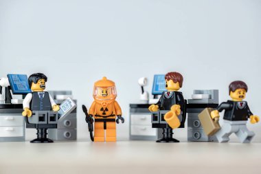 Dört lego ofis çalışanı tehlikeli madde giysisi giymiş ve elinde nükleer tehlike sembolü olan bir meslektaşını görmezden geliyor. İllüstrasyon başyazısı. 20 Ocak 2025
