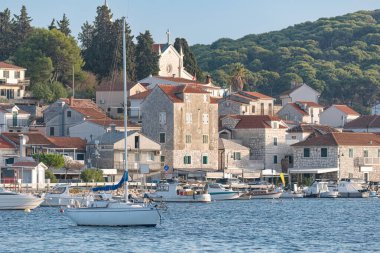 Hırvatistan 'ın Rogoznica limanında huzur içinde yüzen yelkenli, arkasında geleneksel taş evler ve bir kilise bulunuyor.
