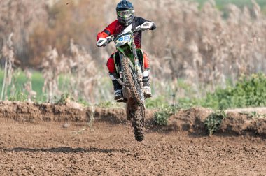 Motokros yarışçısı motorunun ön tekerleğini kaldırarak bir gösteri sergiliyor.